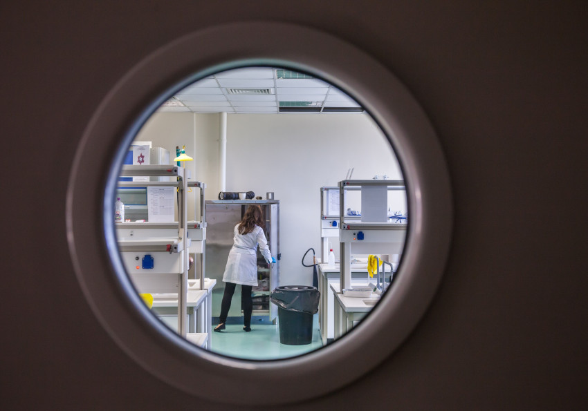 A female scientist in a lab coat working inside a state-of-the-art laboratory through a circular window view.